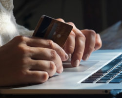 person using laptop, holding credit card, purchasing online